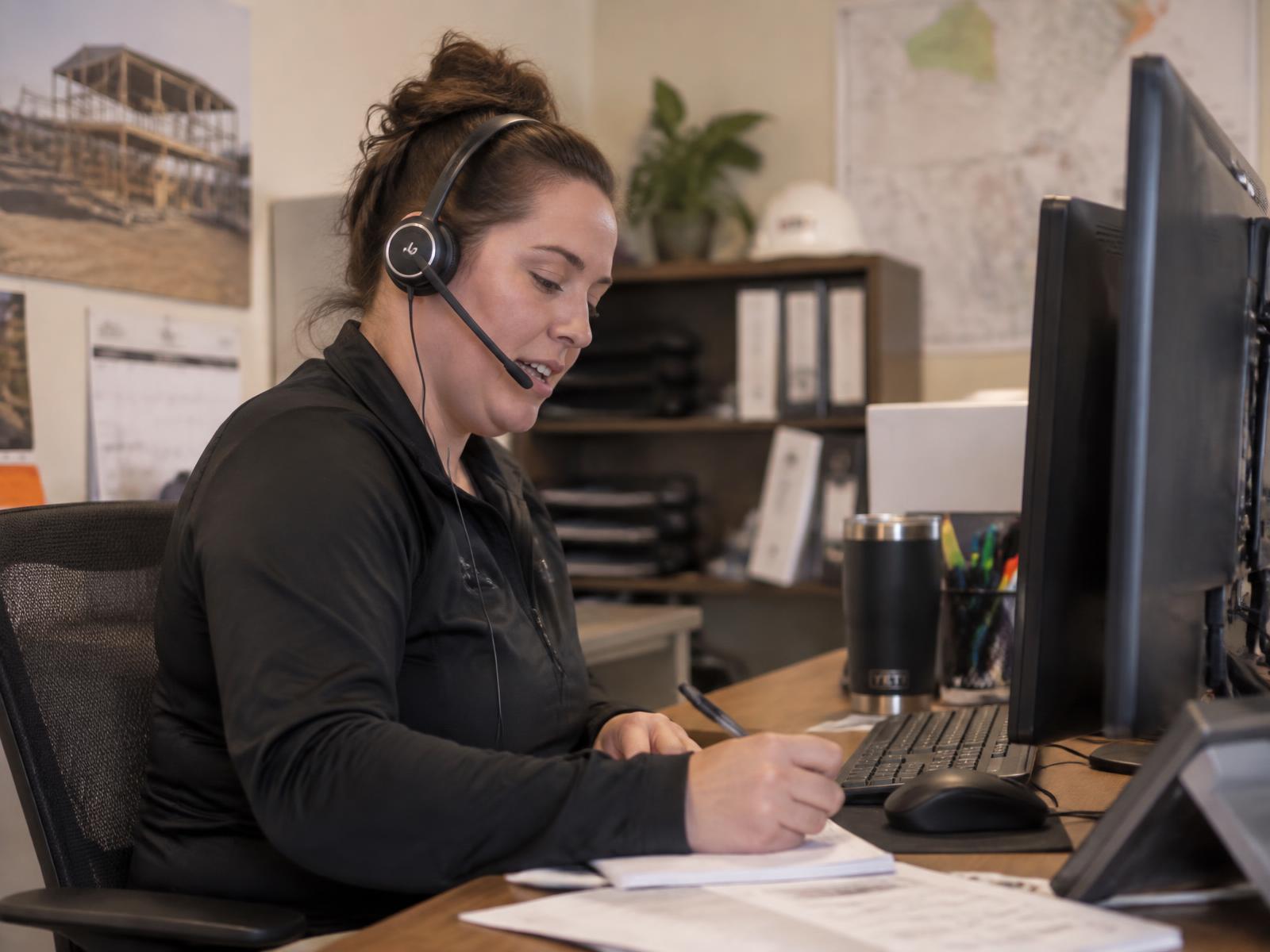 Construction office coordinator on a headset call confirming a project date with a customer